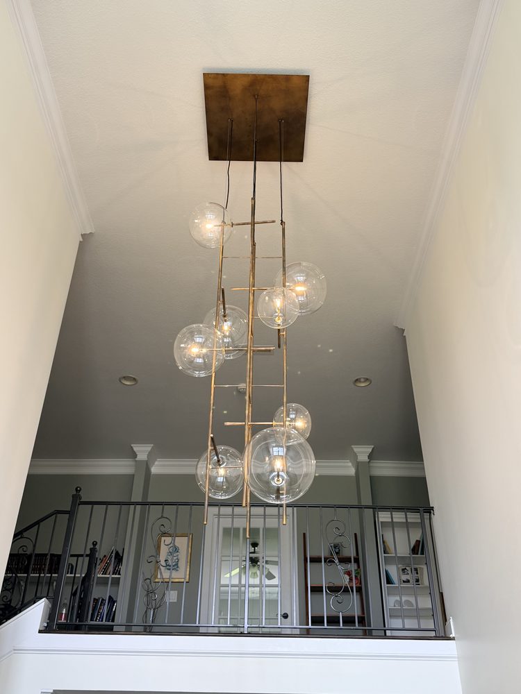 Tall glass-globe chandelier hanging in a two-story foyer below a wood ceiling plate
