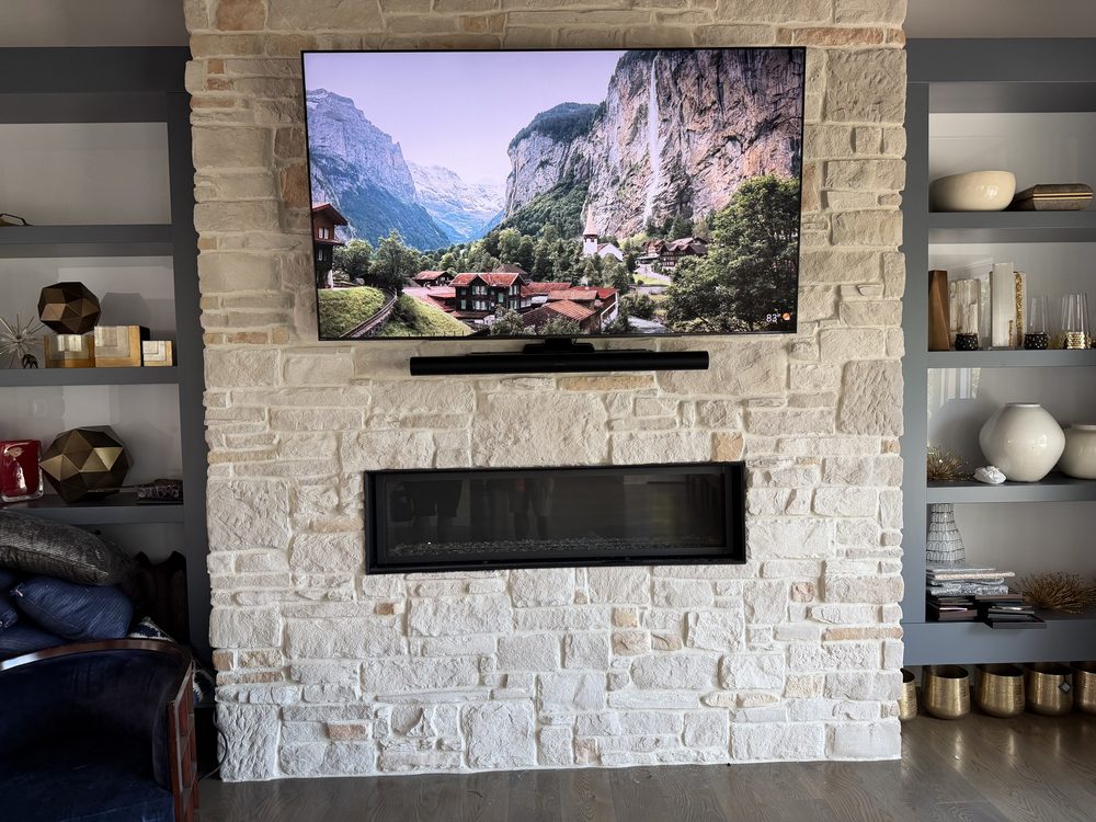 Wall-mounted TV above a linear fireplace on a stacked-stone wall between built-in shelves