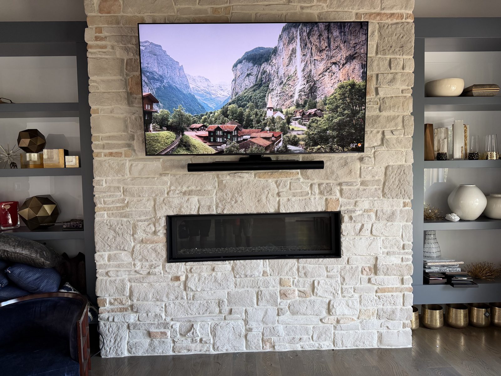 Living room with a white stacked-stone fireplace, linear fireplace insert, wall-mounted TV with soundbar, and charcoal built-in shelves